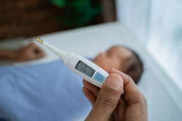 Father measuring temperature to her little baby daughter at home