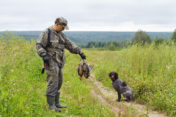 hunter with a gundog and prey is on the field road