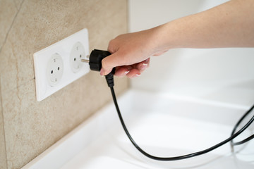 Close up Woman hand insert or pull out elecrticity plug in outlet on the wall