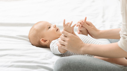 Mother massaging cute newborn baby, doing exercises for his development.