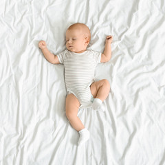 Adorable newborn baby napping on white blanket with arms up