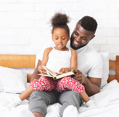 African american man reading book with his cute little daughter