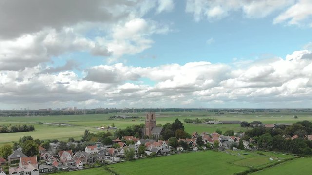 Aerial tilt up showing the village of Ransdorp with its agrarian surroundings and the city of Amsterdam in The Netherlands in the background against a blue sky with clouds