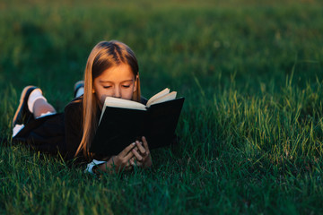 A child lies on the grass and reads a book in the sunset light.