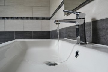 Open chrome faucet washbasin. A stream of water flows into the sink.