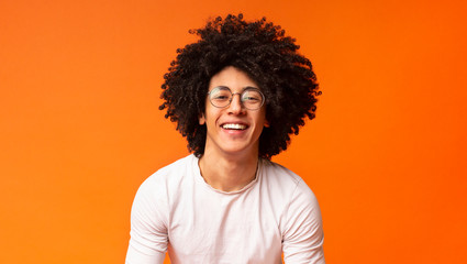 Happy millennial black guy laughing on orange background