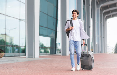Happy man walking with luggage near modern airport building