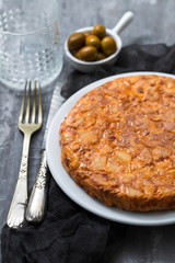 Traditional spanish food Tortilla with potato on white dish and olives in small bowl on ceramic background.