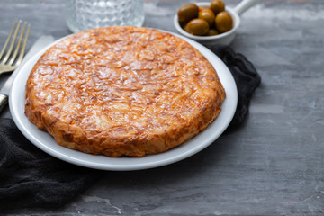 Traditional spanish food Tortilla with potato on white dish and olives in small bowl on ceramic background.
