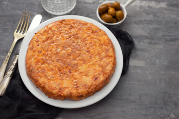 Traditional spanish food Tortilla with potato on white dish and olives in small bowl on ceramic background.