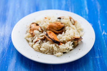 rice with mussels on small white plate on blue wooden background