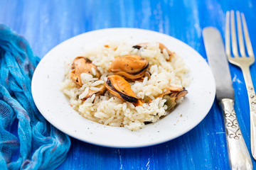 rice with mussels on small white plate on blue wooden background