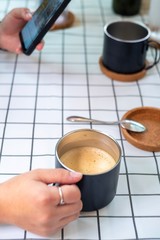 Hand of people holding a black cup of latte coffee and using smartphone on white grid table background , coffee break time relax and refresh.