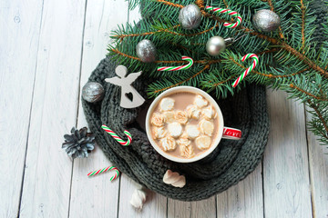  A cup of hot cocoa or chocolate with marshmallows on a background of a knitted scarf and a branch of a Christmas tree. A traditional drink for the Christmas holidays. Top view.
