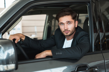 handsome man sitting in brand new car after succesful deal in dealership center feeling happy