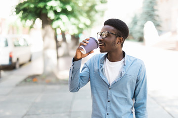 Portrait cool african man drinking coffee holding phone in hand standing on city street