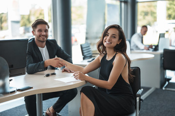 handsome smiling man manager shaking hands with beautiful woman client at dealership office after holding successful deal