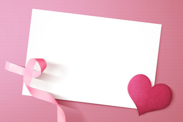 Pink heart and awareness ribbon with empty white paper on a colored background
