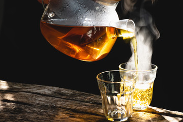 The steam from a cup or pot of coffee or tea on the old wood table and black background, Warm drinks make good healthy, Selective focus.