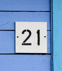 Arabic figure 21 (twenty one) painted with black on a white square plate affixed on an old wooden wall covered with blue paint