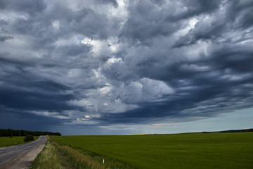 country road along the field under heavy clouds