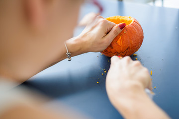 A woman carves her face on a pumpkin for a Halloween lamp on a black table. Close-up female hands making Jack-o'-lantern to the eve of all saints..