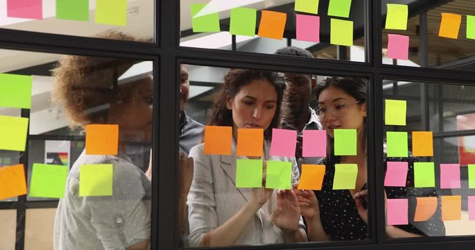 Female mentor teach multiethnic team write tasks on sticky notes
