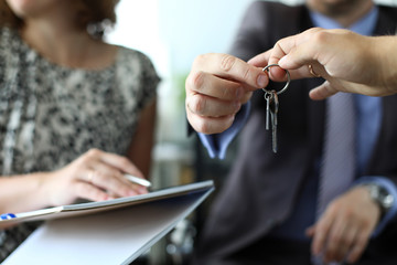 Businessman giving house keys to new owner after signing profitable contract. Woman holding papers...