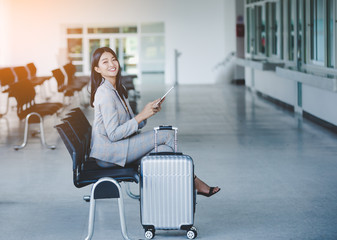 Portrait of business woman looking digital tablet with white travel bag While waiting to travel to the destination