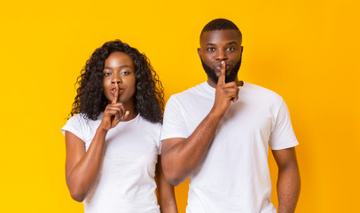 Amazed black couple make silence sign, keep forefingers on lips
