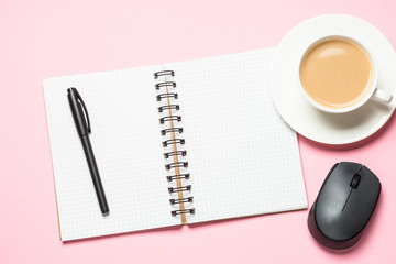 Office workplace with notepad, coffee cup and keyboard on pink background.