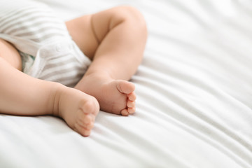 Tiny legs of newborn baby lying on bed in bodysuit