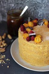 homemade fresh cake decorated with berries and chocolate closeup with a jar of honey and peanuts in the сoncrete background 