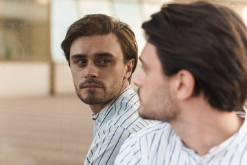 Photo of focused man wearing striped shirt looking at himself in mirror indoors