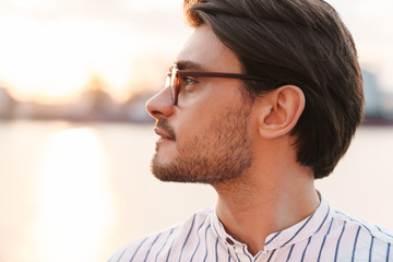 Photo of successful young man standing and looking aside while walking on promenade