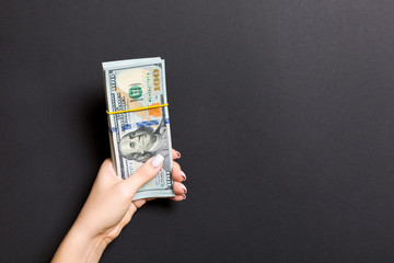 Top view of female hand holding a pack of one hundred dollar bills on colorful background. Wage and...