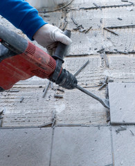 construction worker using a handheld demolition hammer and wall breaker to chip away and remove old floor tiles during renovation work © makasana photo