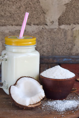Coconut milk in bottle with broken coco on wooden background. Delicious milk cocktail. Copy space.