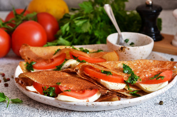 Pancakes with mozzarella and tomatoes with pesto on the kitchen table. Pancakes with caprese.