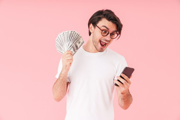 Image of amazed happy man wearing eyeglasses holding cash money and using cellphone