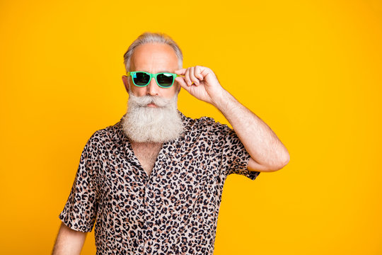 Photo of serious confident old man holding his glasses staring into camera while isolated with yellow background