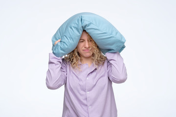 Tired young woman with pillow tries to sleep some more, does not want to get up. Negative facial...