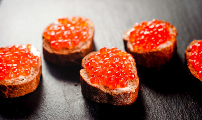 Red caviar on bread on slate background.