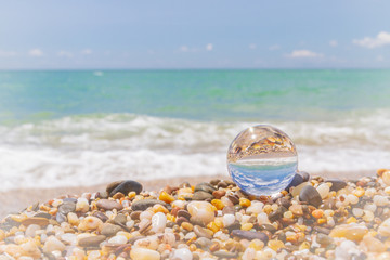 Glass round ball on the beach reflects the sea in summer