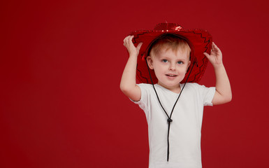 Little kid boy in red festive carnival shiny hat and white t-shirt on a red isolated background. Christmas and New Year concept
