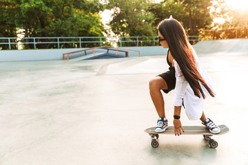 Photo of concentrated young woman riding skateboard in concrete park