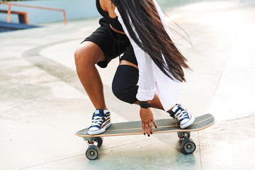 Cropped photo of caucasian young woman riding skateboard in skate park