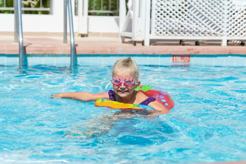 Lovely girl swimming in an outdoor pool with a rubber ring and funny goggles for swimming