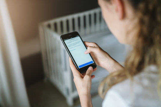 Top view, close-up is smartphone in female hands. In background crib in soft focus. Mom businesswoman works remotely.