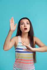 Fototapeta premium Brunette woman with long hair, dressed in colorful striped shirt, posing against blue studio background. Sincere emotions. Close-up.